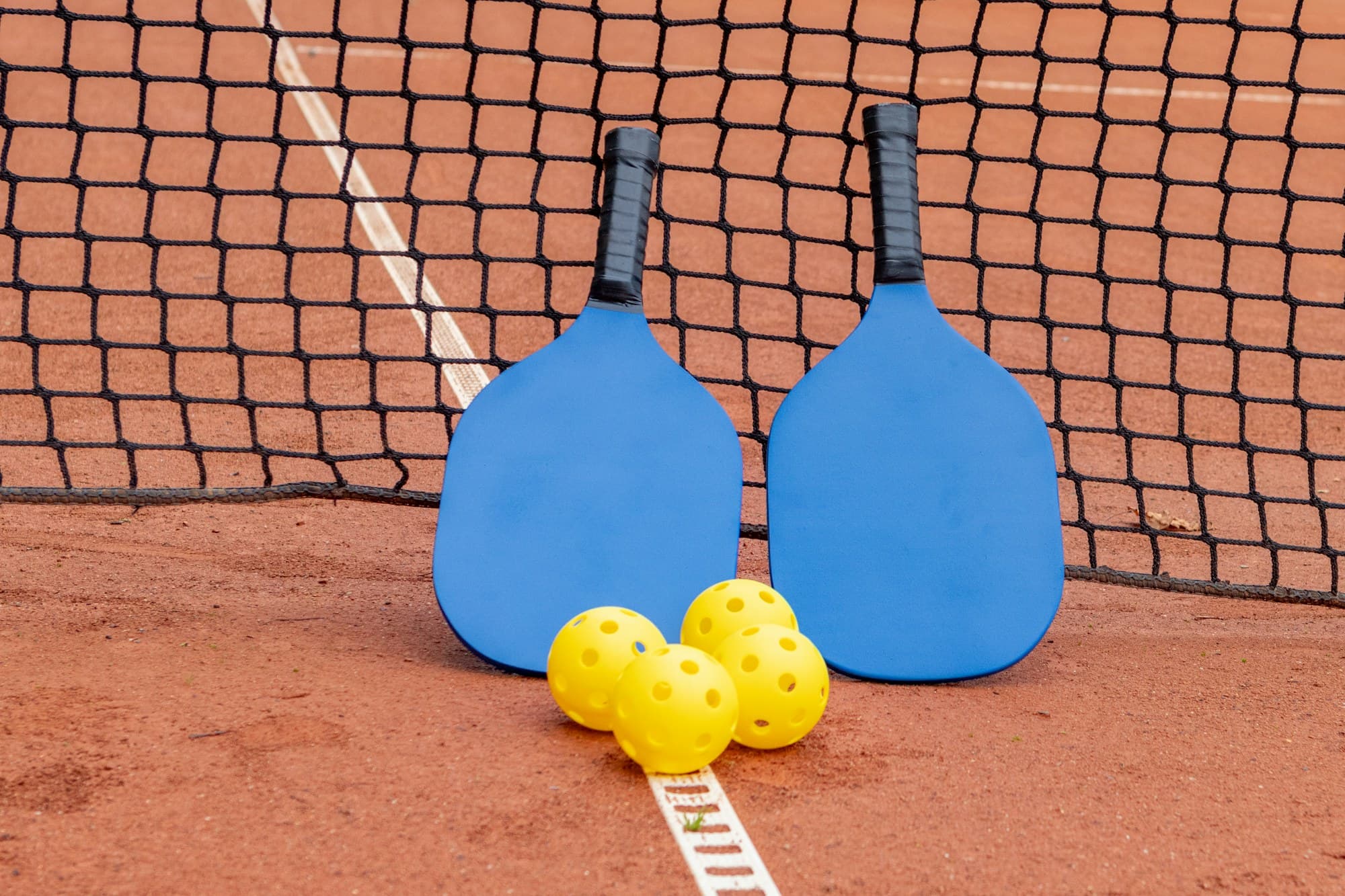 Pickleball paddles and balls resting against the net on an outdoor court